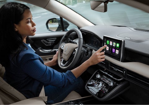 A woman in the driver's seat of a 2022 Lincoln Corsair is touching the center digital screen to connect to Apple CarPlay® | Pugmire Lincoln of Marietta in Marietta GA