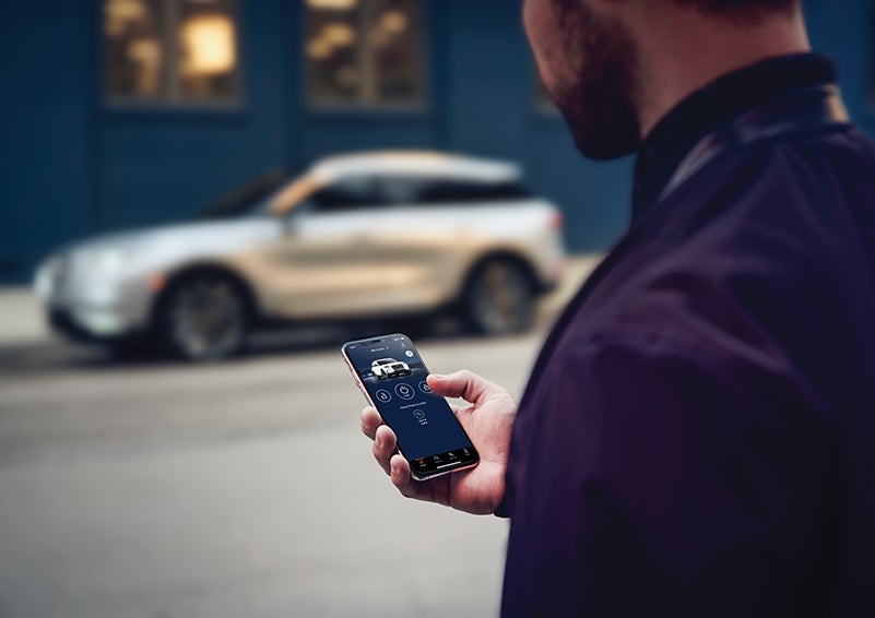 A person is shown interacting with a smartphone to connect to a Lincoln vehicle across the street. | Pugmire Lincoln of Marietta in Marietta GA