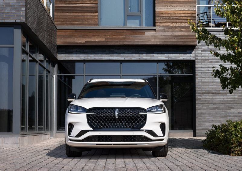 A white 2025 Lincoln Aviator® SUV is shown parked outside a modern building with gray brick and wood accents. | Pugmire Lincoln of Marietta in Marietta GA