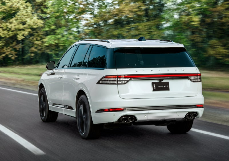 A white 2026 Lincoln Aviator® SUV is being driven away down a road lined with colorful trees. | Pugmire Lincoln of Marietta in Marietta GA