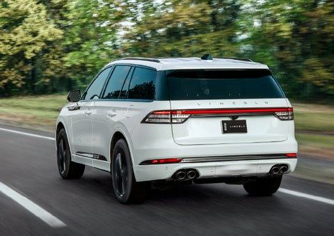 A white 2026 Lincoln Aviator® SUV is being driven away down a road lined with colorful trees. | Pugmire Lincoln of Marietta in Marietta GA