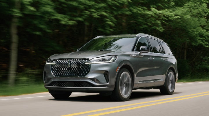 A 2027 Lincoln Aviator® SUV is being driven down a road lined with trees. | Pugmire Lincoln of Marietta in Marietta GA
